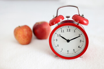 Red alarm clock standing on white towel near apple closeup