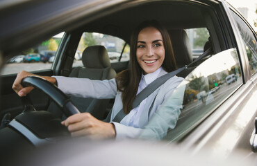 Beautiful happy successful businesswoman is driving a new modern car in good mood. Portrait cute...