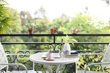 White Coffee cup and laptop and with plants on white metal table at balcony