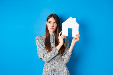 Real estate. Sad frowning girl looking aside with unfair and upset face, showing paper house...