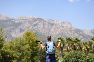Man with backpack holding walking sticks around his neck and admiring mountains back view