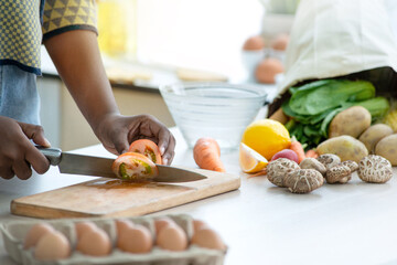 Close up of dark skinned girl hands is preparing fresh salad in kitchen at home, woman cutting tomato