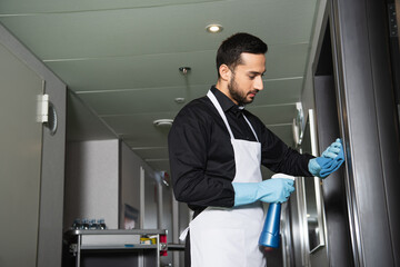Naklejka na ściany i meble bearded housekeeper in rubber gloves cleaning corridor in hotel
