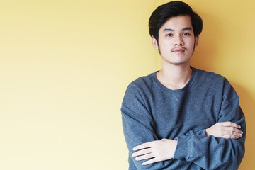 Asian wearing a gray sweater handsome young man smiling indoors with yellow background concept.  