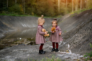 Two three-year-old girls among the gray rocky slopes in a fairy-tale forest hold their favorite...