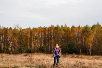 Defocus happy blond 40s woman standing in yellow autumn forest nature background. Happy beautiful lady. Women wearing purple sweater. Fall park, leaves. Dry grass. Out of focus