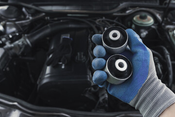 master in glove holds lever silent block in his hand against background of engine. rubber metal...