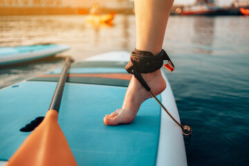Close up of female legs standing on blue yellow color SUP stand up paddle board or surfboard puts...