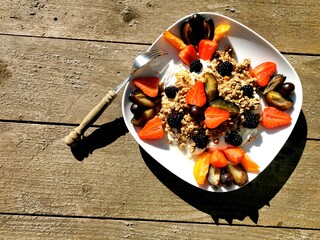 A plate on a wooden surface with cereals, yogurt and fruit.