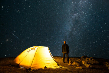 Traveler near the glowing camping tent on the background of the starry sky with milky way. 