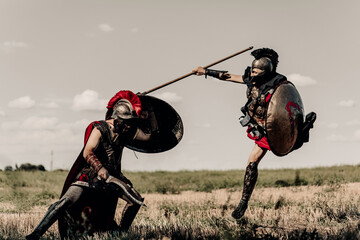 Battle with spear and sword between two ancient warriors in battle dress on meadow.