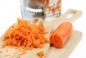 Chopped and half of carrots on wooden cutting boards and grater on the background