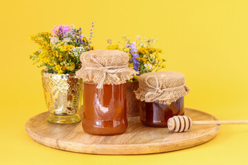 Jars with honey and bouquets of wild flowers on a yellow background.