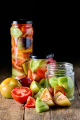 Glass jars with preserved tomatoes and some fresh tomatoes