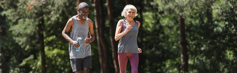Positive interracial couple jugging together in forest, banner.