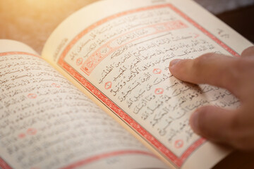 Quran (Koran) - close up of holy book of Muslims, with hand pointing ayat (Āyah), and shining light.