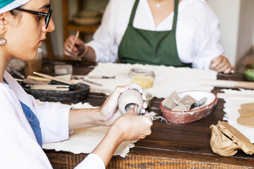 female hands on the table create a ceramic piece, close-up, daylight, shooting from above and from the side