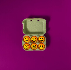 Halloween pumpkins made of orange ping-pong balls in a cardboard egg box with a purple background. Minimal concept.