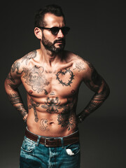 Fototapeta premium Portrait of handsome confident stylish hipster lambersexual model. Sexy modern man. Naked torso with tattoos.Fashion male posing in studio on dark background. In sunglasses