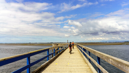 Naklejka premium Cyclists on Blackie Spit pier at Crescent Beach, Surrey, BC, on an overcast summer day.