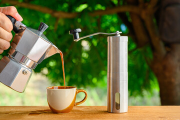 Boran coffee brewing that grinds coffee beans by hand Italian Moka pot with hot cups of coffee and coffee beans sprinkled on a wooden table.