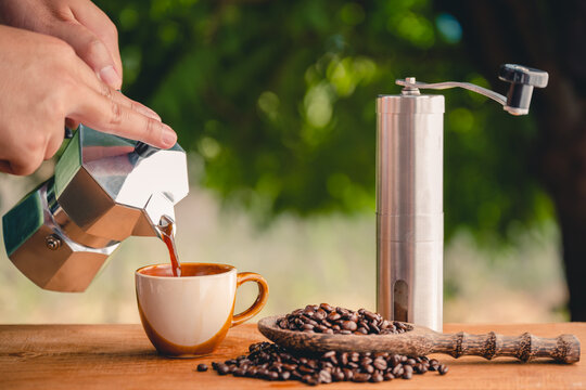 Boran coffee brewing that grinds coffee beans by hand Italian Moka pot with hot cups of coffee and coffee beans sprinkled on a wooden table.