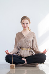 A young attractive girl is meditating while sitting in a lotus on the floor with a burning aroma....