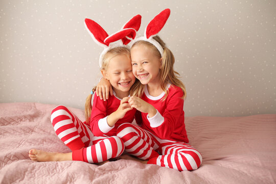 girls sisters blonde sitting at home on the bed in red pajamas and bunny ears