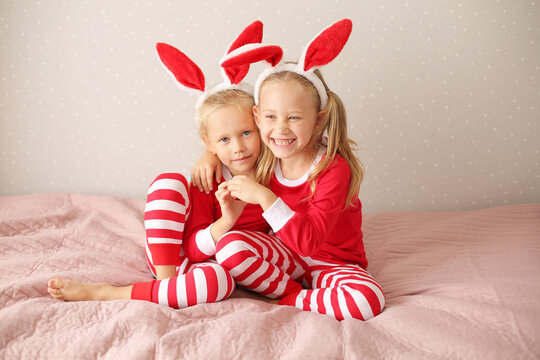 girls sisters blonde sitting at home on the bed in red pajamas and bunny ears