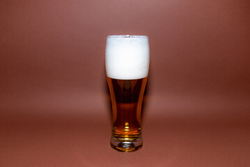 One Glass beer on brown background with copy space.Amber glass beer with foam. brown background.Selective focus.