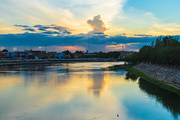 Fototapeta premium Ratchaburi, Thailand - June 20, 2020 : Residence, business buildings, market and public garden beside the river in a cloudy day sunset.