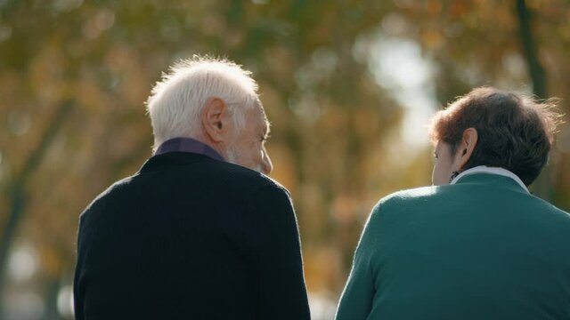 4k Back view of happy lovely caucasian senior couple sitting in bench and hugging each other . Rear view of romantic old couple sit on bench and enjoy in the open air . Happiness people .  Slow Motion