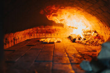 Closeup shot of pieces of bread baking in a stone oven with big fire