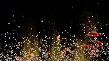 Mixture of ground spices, assorted peppers, salt and small red chili peppers slowly rise and fall against a black background. 300fps