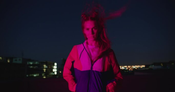 portrait teenage girl posing in city at night looking confident with urban style in red light wind blowing hair