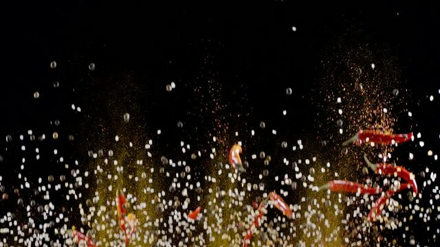 Mixture of ground spices, assorted peppers, salt and small red chili peppers slowly rise and fall against a black background. 300fps