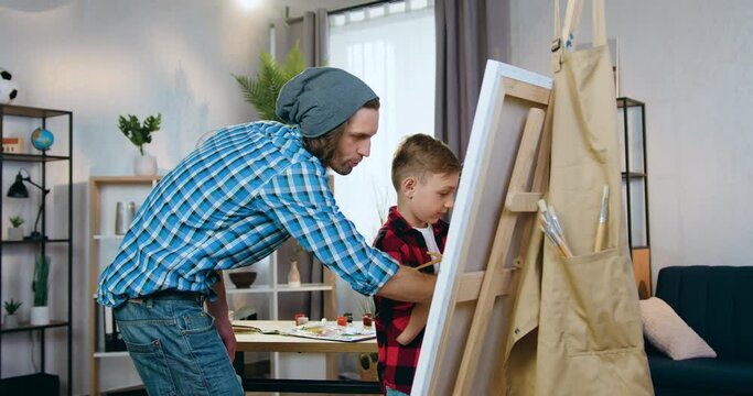 Attractive creative young male artist teaching small boy to draw picture in workshop,art concept