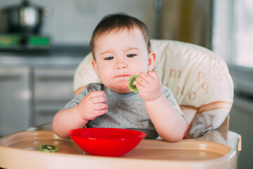 little girl on a high chair eating kiwi