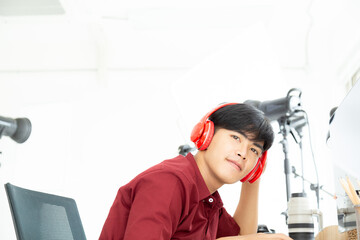 Fototapeta na wymiar Portrait young happy asian photographer in red shirt working and listening music from red modern head phone in his studio.