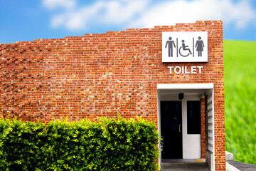 Fototapeta na wymiar The red brick public restroom with symbols for men, women, and people with disabilities is designed for a universal design against a backdrop of blue sky and white clouds.