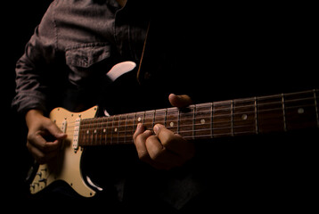 Plakat Guitarist holding electric guitar in hand and strumming chord on black background.