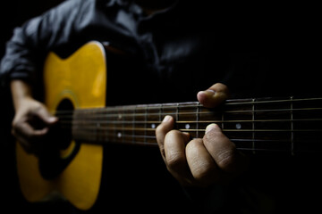 Left-handed focus of a guitarist holding an E major middle position chord on a black background.