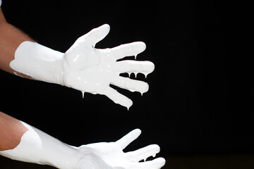 White paint flows from the fingers on a black background