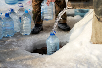 A man draws water from an icy drinking spring. There are a lot of plastic containers with collected...