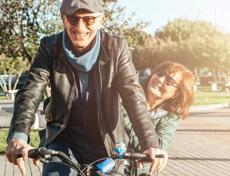Retired couple enjoying free time walking with bicycle - middle-aged couple having fun and smiling together riding a bike - warm contrast filter.