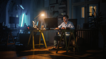 Focused and Productive Man Works on a Desktop Computer in Creative Agency in Dark Loft Office in...