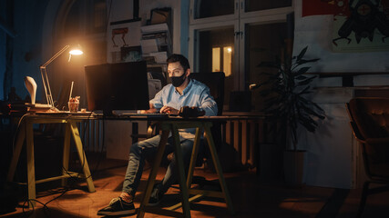 Stylish Male Employee Wearing Protective Face Masks while Working on Computer in Creative Agency in Loft Office. Renovated Stylish Design with House Plants Artistic Posters. Pandemic Covid-19 Concept.