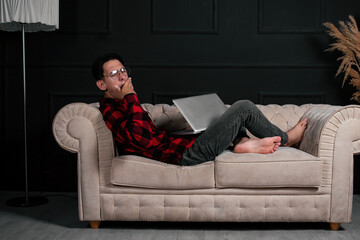 An intelligent and handsome student learns remotely at home while lying on the couch. Online...