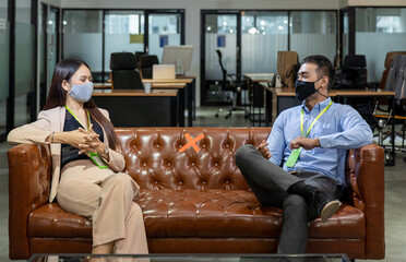 Asian male and female corporate colleagues wearing protective medical face mask sitting and discussing on sofa in office during to coronavirus, or COVID 19 outbreak. Business, new normal concept