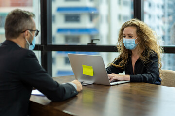 Business man and business woman wearing protective medical face mask, wearing formal suite, sitting and working with computer laptop in the modern office. health, businesspeople and office concept